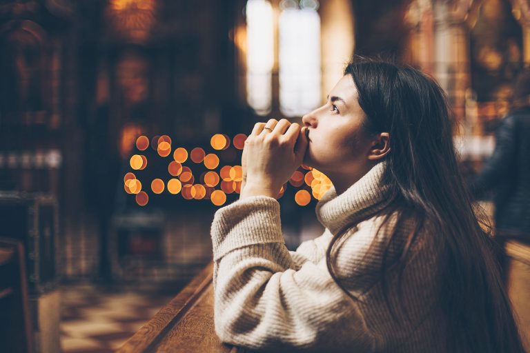 The parishioner of the church sits on a bench with her hands folded for prayer and heartily prays.