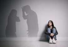 Upset teenage girl sitting on floor near wall and silhouettes of arguing parents